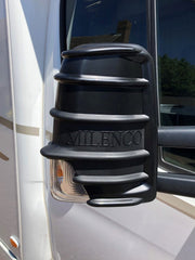 Black Milenco mirror protector fitted to a motorhome cab mirror, close-up with embossed logo