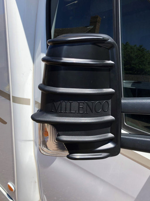 Black Milenco mirror protector fitted to a motorhome cab mirror, close-up with embossed logo