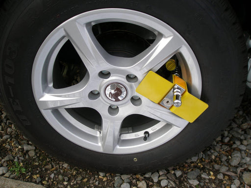 Yellow Milenco Compact C wheel clamp locked onto an alloy wheel outdoors