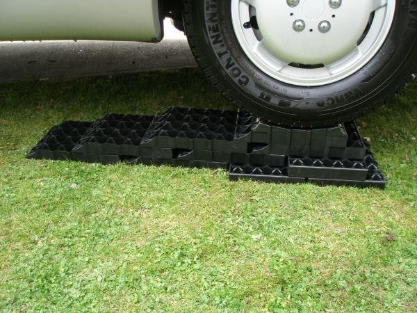 Milenco Stacka Level blocks stacked into a ramp under a caravan tyre on grass